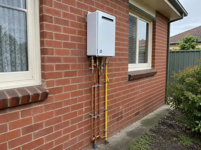 Wall mounted hot water unit with exposed copper and yellow pipes on a brick house in Telarah