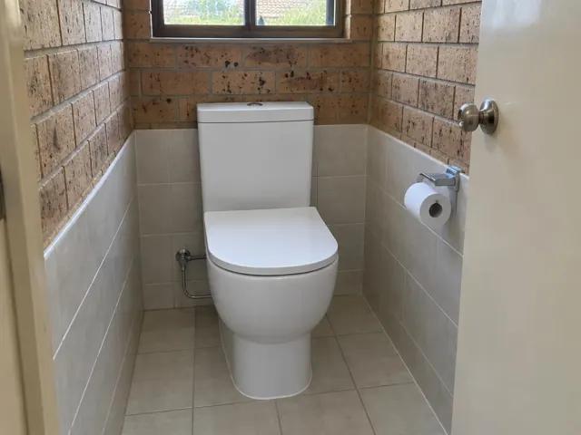 White toilet in a tiled small bathroom with brick walls and a window in Oakhampton Heights